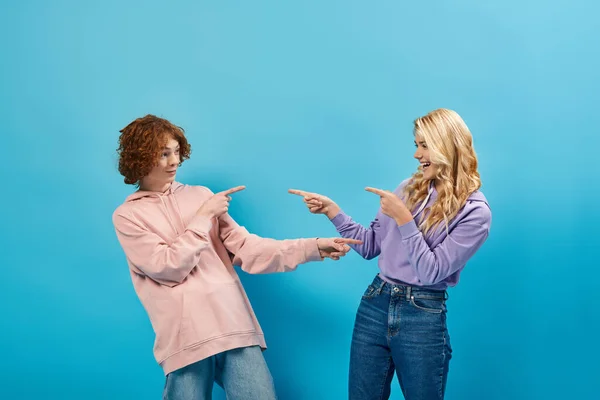 Веселые подростки в стильных нарядах, указывающие пальцами и друг на друга и смеющиеся над синим — стоковое фото
