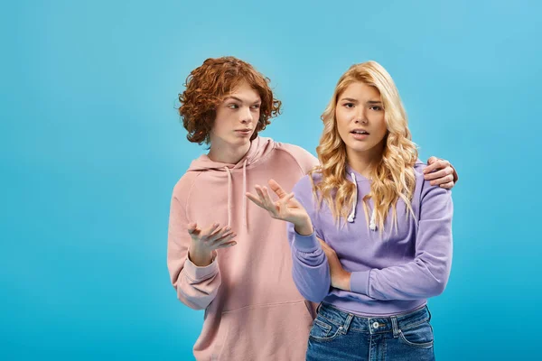 Redhead teenage boy embracing and calming frustrated blonde girlfriend on blue, unity and support — Stock Photo