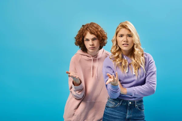 Missbilligte Teenager-Jungen und -Mädchen in stylischen Kapuzenpullovern, die mit den Händen zeigen und in die Kamera auf blau schauen — Stockfoto