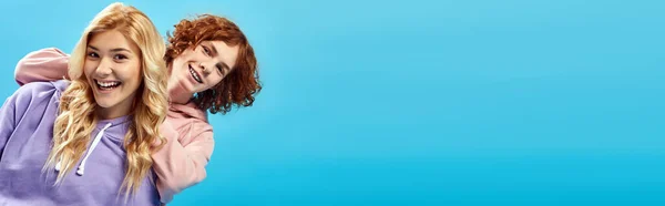 Blonde teenage girl with redhead having fun in studio and laughing at camera on blue, banner — Stock Photo