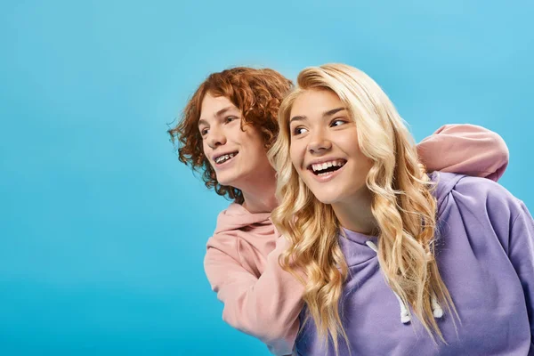 Despreocupados amigos adolescentes con ropa casual elegante sonriendo y mirando hacia otro lado en azul, felicidad - foto de stock