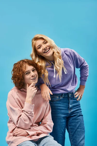 Cheerful teenage couple of friends in stylish hoodies posing and smiling at camera on blue — Stock Photo
