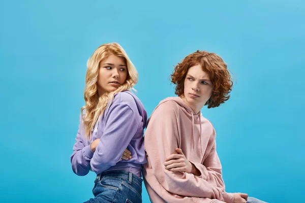 Offended teenage friends with folded arms sitting back to back and looking at each other on blue — Stock Photo