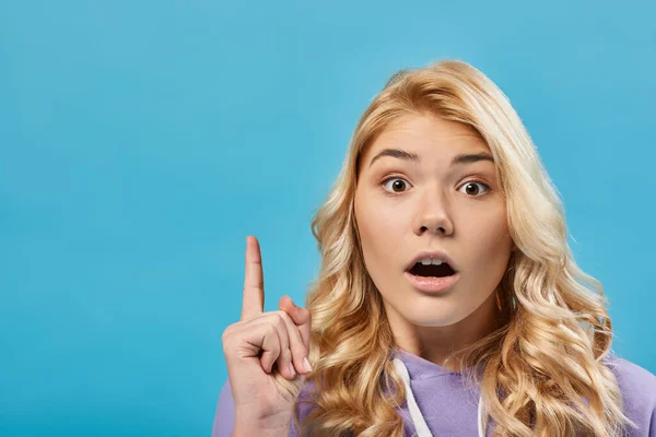 Retrato de adolescente rubia sorprendida con la boca abierta mostrando gesto de idea en azul - foto de stock