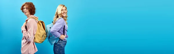 Lächelnde Teenager in trendigen Kapuzenpullovern, Rücken an Rücken mit Rucksäcken auf blauem Banner — Stockfoto