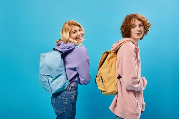 Despreocupados estudiantes adolescentes en sudaderas con capucha de moda posando con mochilas y mirando a la cámara en azul - foto de stock