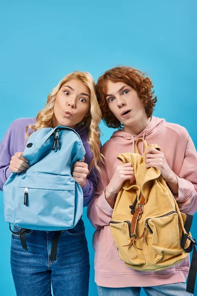 Asombrado adolescentes estudiantes en sudaderas con capucha de moda celebración de mochilas y mirando a la cámara en azul - foto de stock