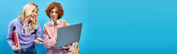 Щаслива дівчина-підліток з смартфоном і блокнотом, дивлячись на ноутбук поруч з рудим другом на синьому, банер — стокове фото