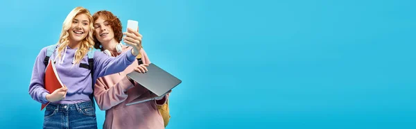 Allegra ragazza adolescente con notebook scattare selfie con studente rossa che tiene il computer portatile su blu, banner — Foto stock