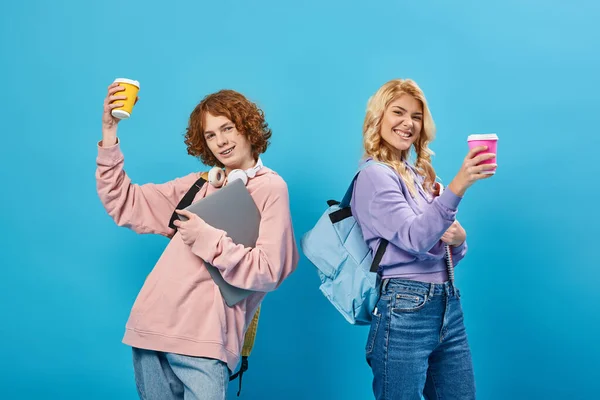 Gioiosi studenti adolescenti con zaini e tostatura portatile con bicchieri di carta, sorridenti alla fotocamera blu — Foto stock