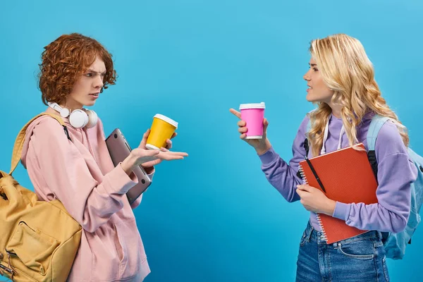 Unzufriedene Teenager-Freunde mit Rucksäcken und Pappbechern, die auf einander zeigen und sich auf blau zanken — Stockfoto