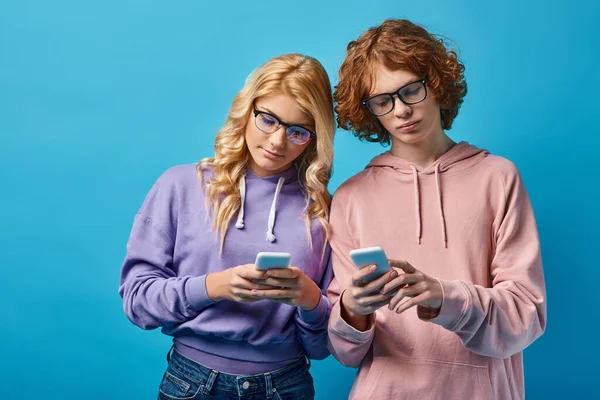Teenager-Freunde in Brillen und trendigen Kapuzenpullovern vernetzen sich auf Smartphones auf blauem Grund, Generation z — Stockfoto