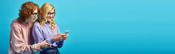 Sorrindo menina adolescente loira em óculos de rede no smartphone perto de ruiva amigo em azul, banner — Fotografia de Stock