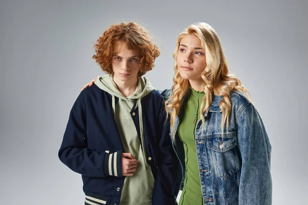 Selbstbewusster rothaariger Teenager schaut in die Kamera nahe der blonden Freundin, trendige Teenager-Freunde auf grau — Stockfoto