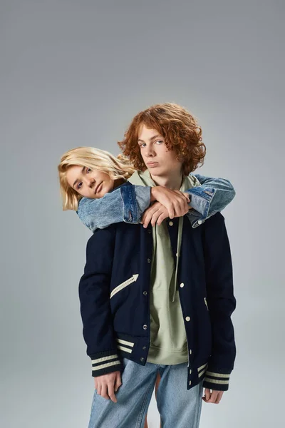 Blonde teenage girl embracing redhead friend wearing trendy casual clothes on grey, youth fashion — Stock Photo