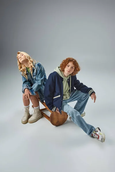 Rothaarige Teenie-Typ in trendiger Freizeitkleidung Blick auf Kamera in der Nähe blonde Freundin sitzt auf grau — Stockfoto