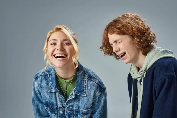 Amigos adolescentes emocionados en elegante atuendo casual riendo mientras posan en el estudio sobre fondo gris - foto de stock