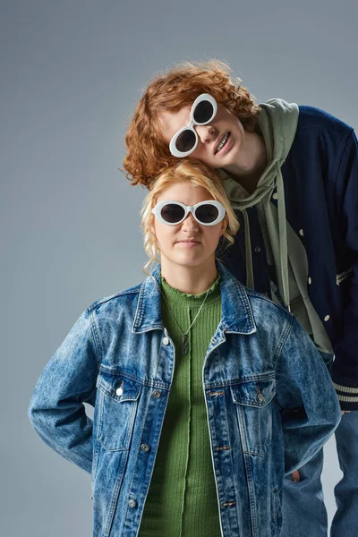 Teenager-Freunde in stylischer Freizeitkleidung und Sonnenbrille blicken in die Kamera, während sie auf grau posieren — Stockfoto