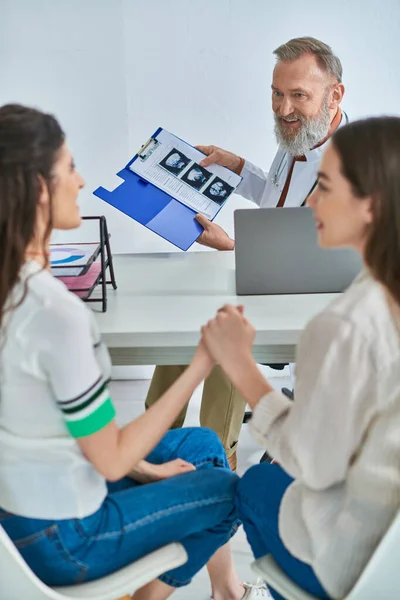 Lgbt couple holding hands looking at each other while gynecologist showing ultrasound, ivf concept — Stock Photo