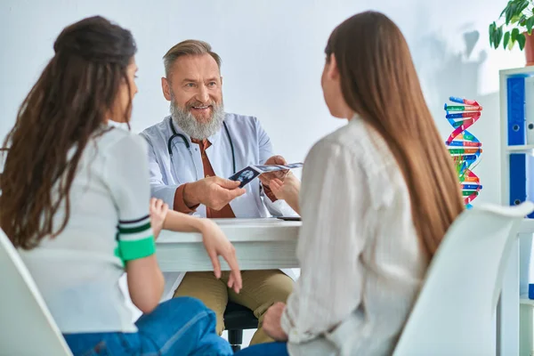 Cheerful grey bearded doctor showing lgbt couple their ultrasound, in vitro fertilization concept — Stock Photo