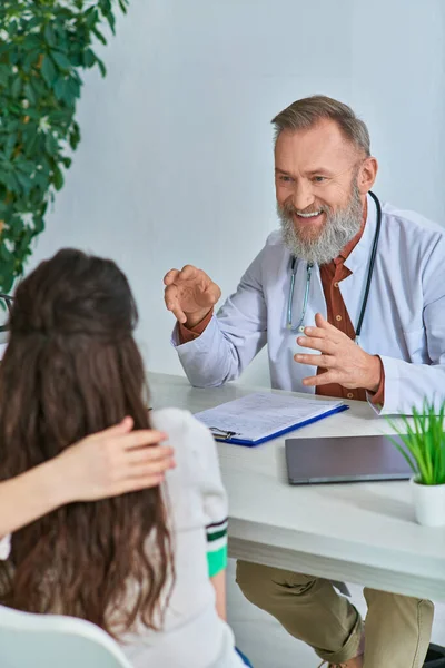 Cheerful grey bearded doctor gesturing and talking joyfully to young lgbt couple, ivf concept — Stock Photo