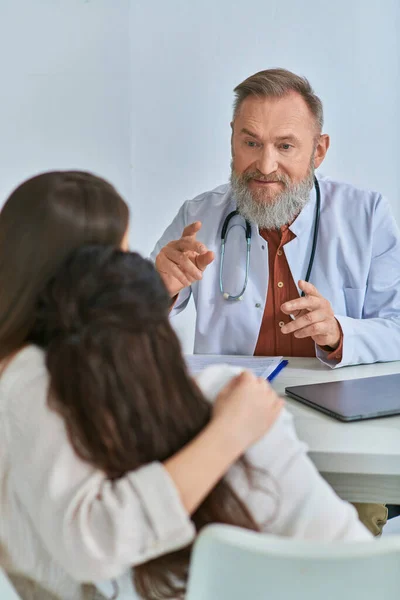 Grey bearded doctor gesturing and explaining something to beautiful lgbt couple, ivf concept — Stock Photo