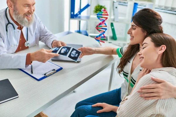 Smiling lesbian couple holding ultrasound of their baby from doctor, in vitro fertilization concept — Stock Photo