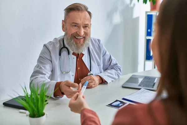 Fröhlicher Arzt lächelt aufrichtig seine brünette Patientin an und zeigt ihm einen Schwangerschaftstest, ivf concept — Stockfoto