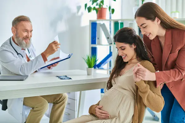 Cheerful lgbt couple having doctor appointment holding hands looking at pregnant belly, ivf concept — Stock Photo
