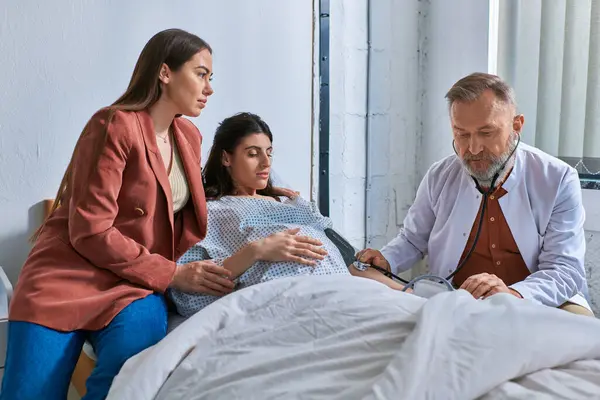Concentrated doctor with tonometer measuring pressure in pregnant lesbian woman, ivf concept — Stock Photo