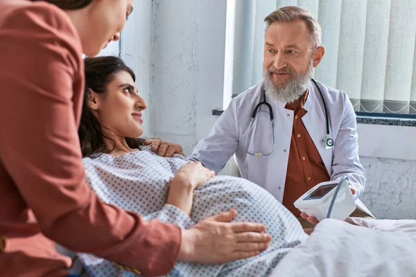 Focused doctor looking at his pregnant patient measuring pressure, hand on shoulder, ivf concept — Stock Photo