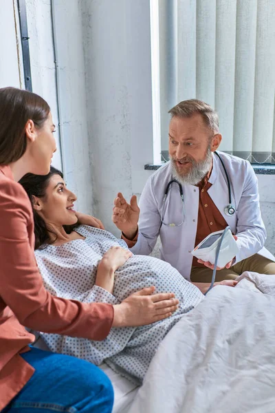 Graubärtiger Arzt, der seiner schwangeren Patientin etwas erklärt, das den Druck misst, ivf concept — Stockfoto