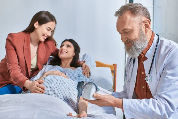 Joyous lgbt couple smiling cheerfully at each other while doctor measuring pressure, ivf concept — Stock Photo
