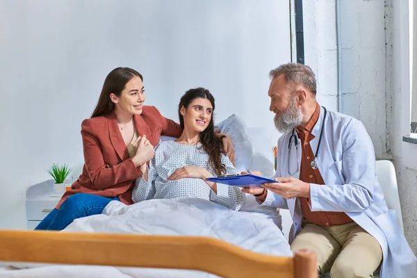 Cheerful lesbian couple having medical check on pregnancy looking at their doctor, ivf concept — Stock Photo