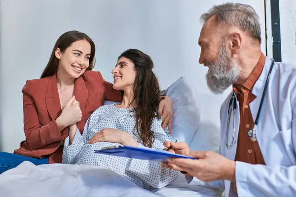 Happy lesbian couple holding hands looking at each other while doctor smiling at them, ivf concept — Stock Photo
