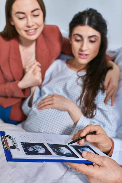 Young lesbian couple looking at ultrasound of their baby child during appointment, ivf concept — Stock Photo