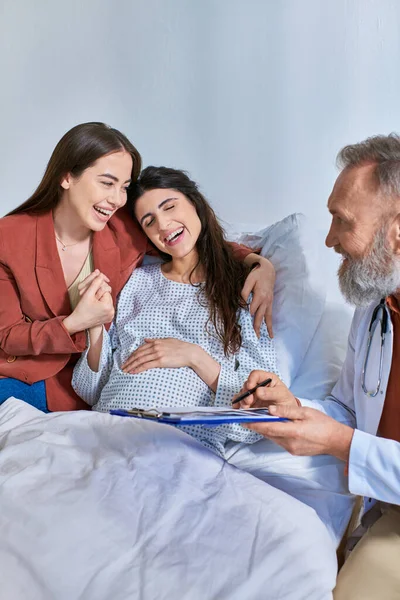 Happy lesbian couple smiling sincerely holding hands while doctor showing ultrasound, ivf concept — Stock Photo