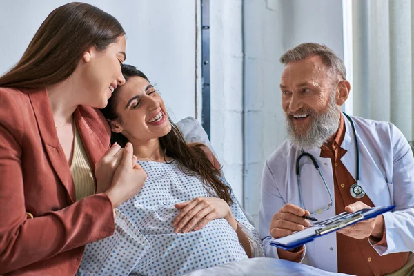 Jolly doctor showing ultrasound to cheerful smiling lesbian couple, in vitro fertilization concept — Stock Photo