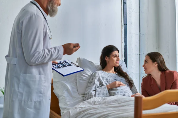 Loving lgbt couple looking at each other at appointment with doctor holding ultrasound, ivf concept — Stock Photo