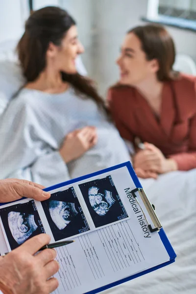 Close up of ultrasound with cheerful lesbian couple smiling at each other on backdrop, ivf concept — Stock Photo
