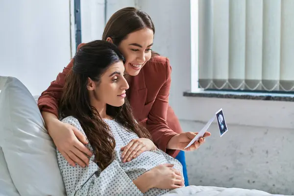 Молода пара лесбіянок, дивлячись на ультразвук своєї дитини руками на вагітному животі, концепція IVf — стокове фото
