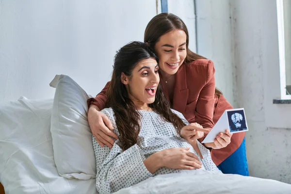 Überraschtes fröhliches lgbt-Paar beim Anblick des Ultraschalls seines Babys mit den Händen auf dem Bauch, ivf concept — Stockfoto