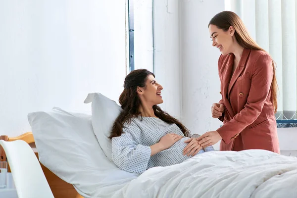 Cheerful lesbian couple at hospital looking happily at each other and holding hands, ivf concept — Stock Photo