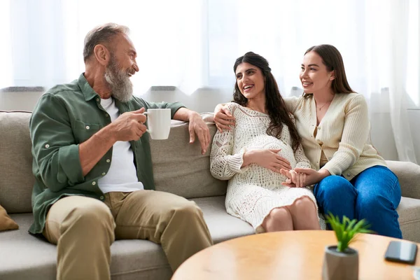 Happy cheerful lgbt couple with father of one sitting on sofa and drinking tea, ivf concept — Stock Photo