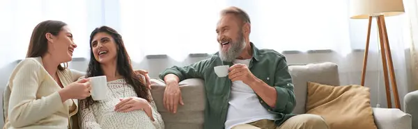 Lgbt couple and father of one of them sitting on sofa laughing and drinking tea, ivf concept, banner — Stock Photo