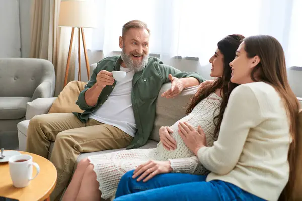 Cheerful father paid visit to his lesbian daughter and her partner sitting on sofa, ivf concept — Stock Photo