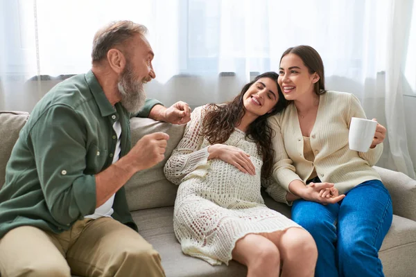 Father talking cheerfully to his pregnant daughter and her partner sitting on sofa, ivf concept — Stock Photo