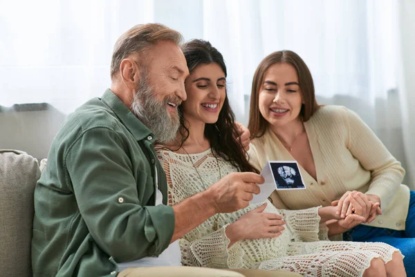 Jolly pregnant daughter showing her father and her cheerful partner ultrasound of baby, ivf concept — Stock Photo