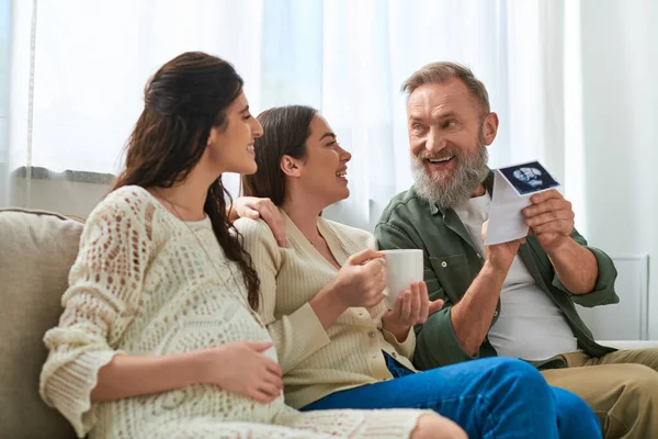 Daughter looking at her partner and father discussing ultrasound sitting on sofa, ivf concept — Stock Photo