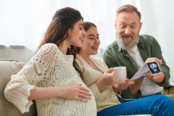 Cheerful lgbt couple and father of one of them drinking tea and discussing ultrasound, ivf concept — Stock Photo